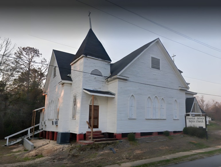 Desegregation Academies: Rundown white clapboard church with gray roof surrounded by unkempt, dried out grass and weeds.