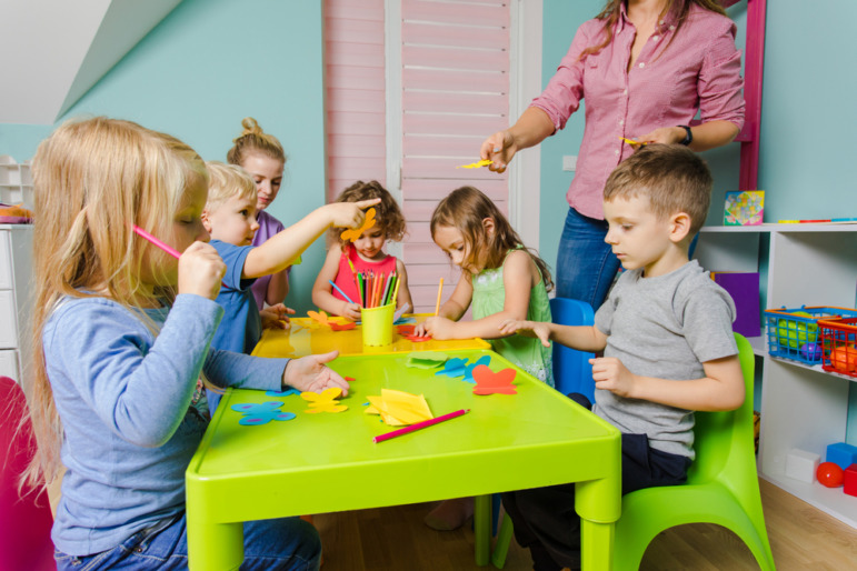 Child care: Group of preschoolers sit doing activties at a green table.