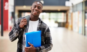 A living stipend for disadvantaged college students: black, male college student smiles while holding folder and walking with backpack on