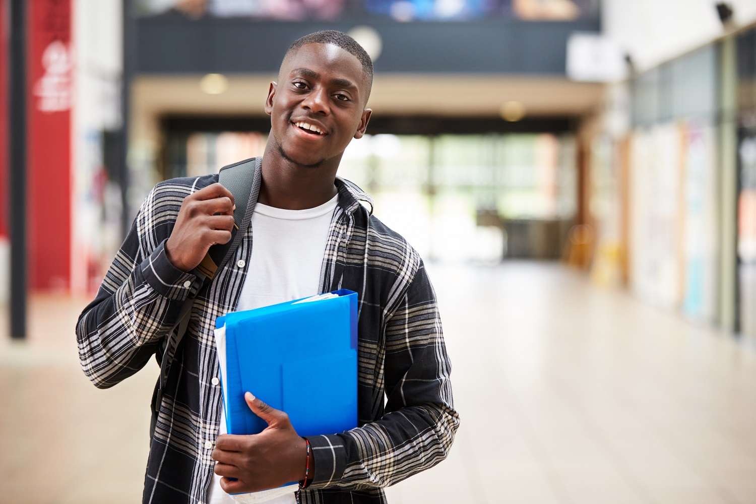 A living stipend for disadvantaged college students: black, male college student smiles while holding folder and walking with backpack on
