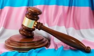 Transgender locker room ruling: Transgender flag with white, pale blue and pale pink stripes sits behind a brown wood courtroom judge's gavel