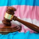 Transgender locker room ruling: Transgender flag with white, pale blue and pale pink stripes sits behind a brown wood courtroom judge's gavel