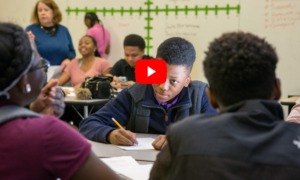 Algebra is a civil right: High school class of several Black students sit at desks woriting on papers with a white board with number lines in the background