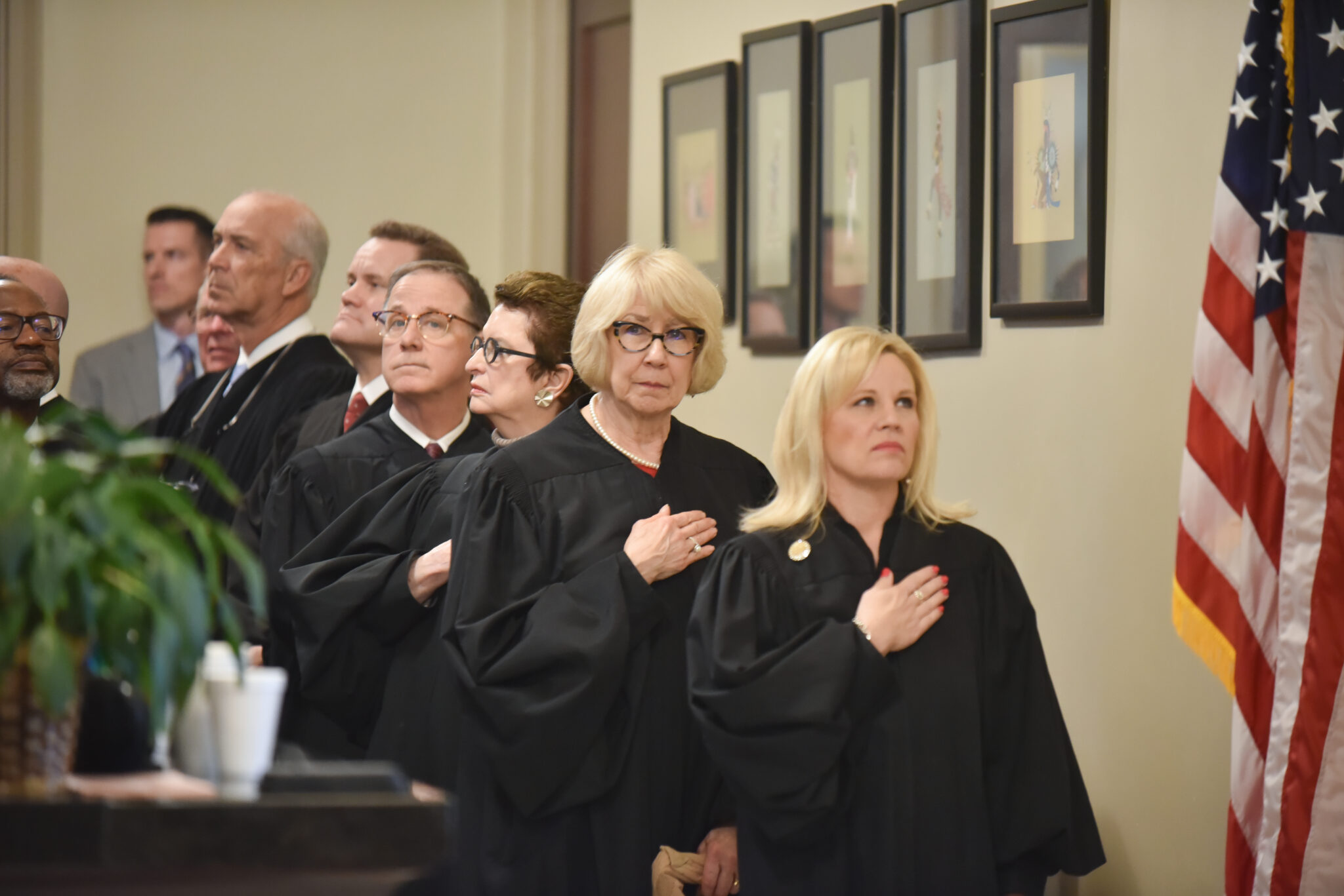 Oklahoma-strikes-down-religious-charter-school: Several people in black judge's robes stand at attention on interior steps with hand over heart facing American flag