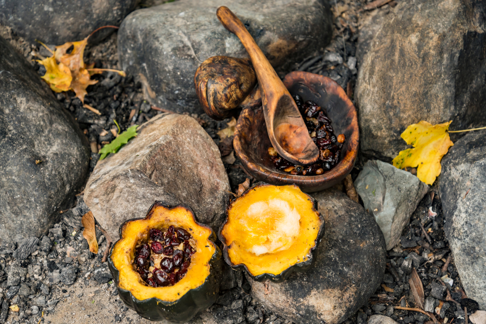 _Native American agriculture: Cooked black and red beans in and round orange squash cut in half, sitting amidst stones in an outdoor firepit