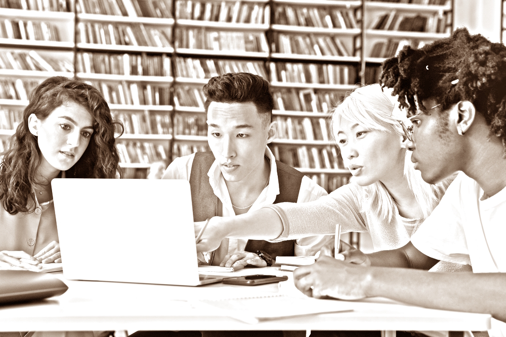 College Essay after affirmative action ended: Four multiethnic schoolmates look at laptop in library discussing information they see on screen