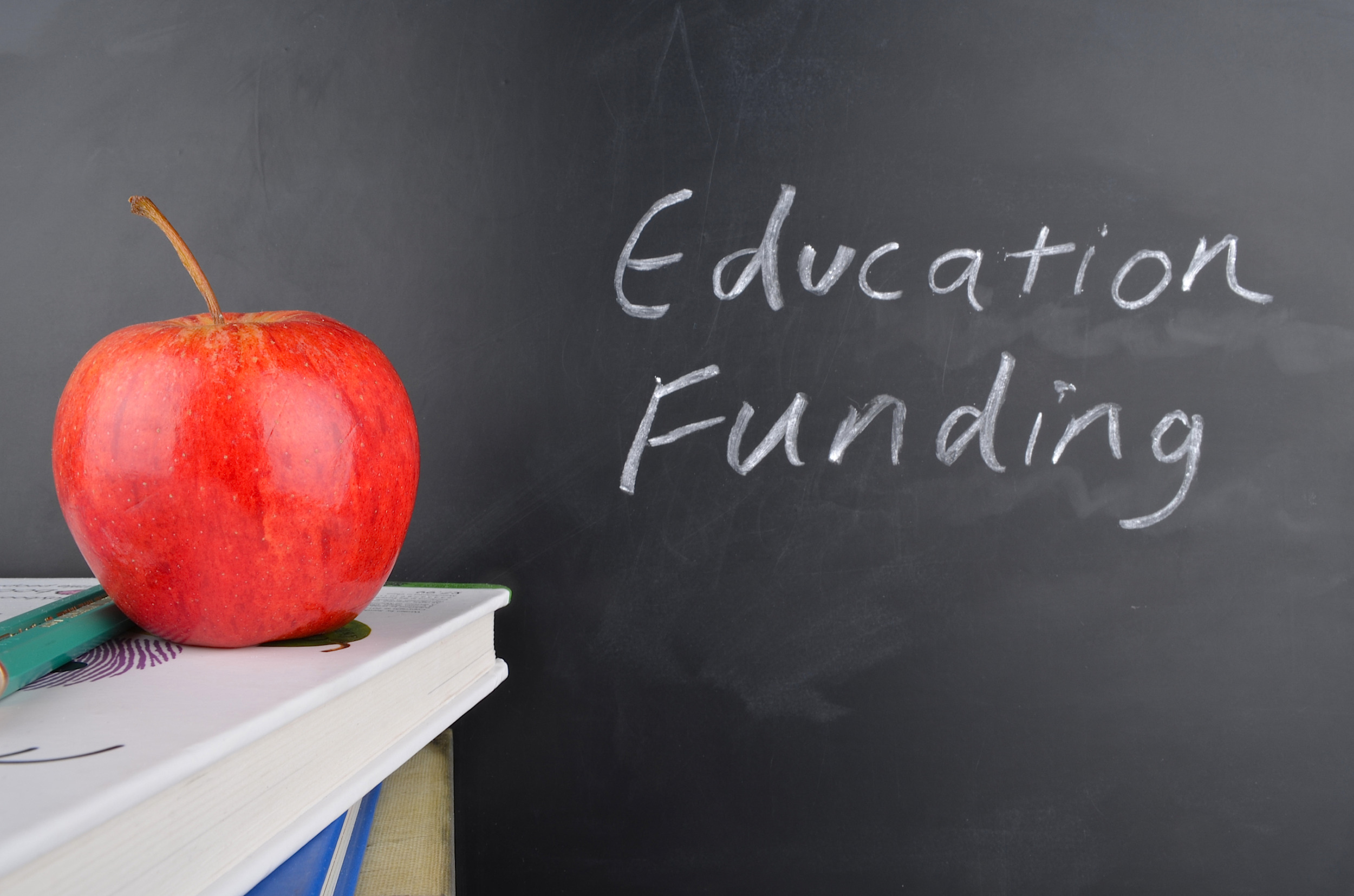 Pandemic school funding: Classroom with red apple,books and handwriting in white chalk on blackboard "Education Funding"