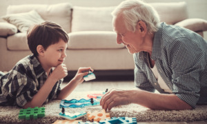 Kinship foster care: Older white-haired man and young boy are playing with toys on the carpeted floor, looking at each other and smiling