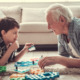 Kinship foster care: Older white-haired man and young boy are playing with toys on the carpeted floor, looking at each other and smiling