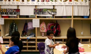 Undocumented students: Three young, dark-haired students sit at low tables in elementary classroom in front of wooden cubbies and colorful alphabet wall decorations