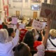 Arming teachers in Tennessee: Back view of several people holding up hand-printed signs seated in second story gallery overlooking government officials in session on first floor