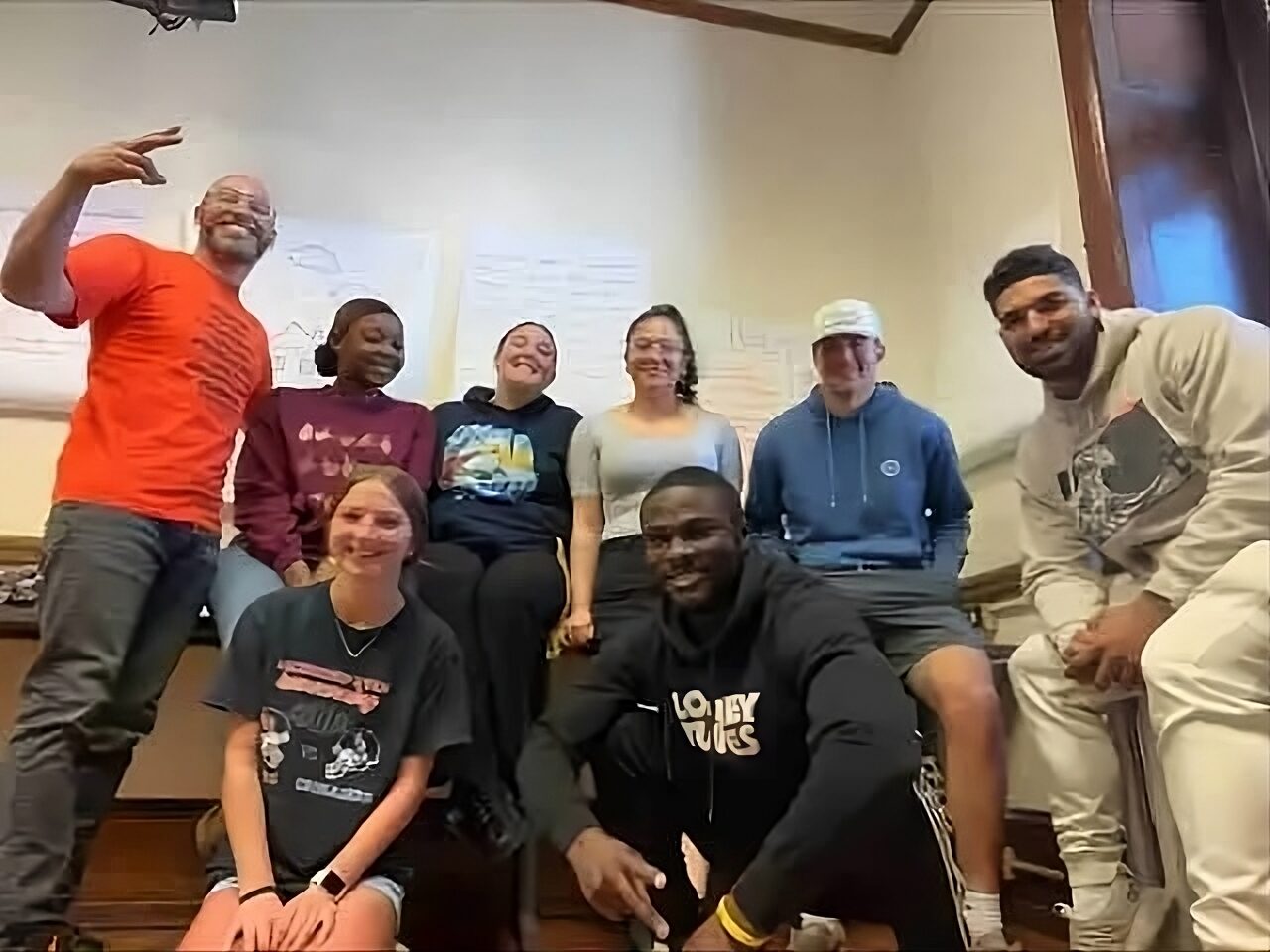 Restorative justice manual:Group of college age adults with older, balding man grouped together , some sitting others standing in back row, in large white room.