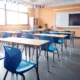 From chronic absence to chosen presence: chronic absenteeism, Classroom with light wood desks and bright blue chairs and no students