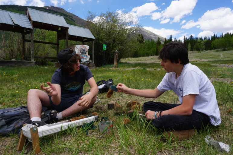 Rural school districts join forces: Two teen boys sit in a grass fiel dgathering soil and ecosystem samples