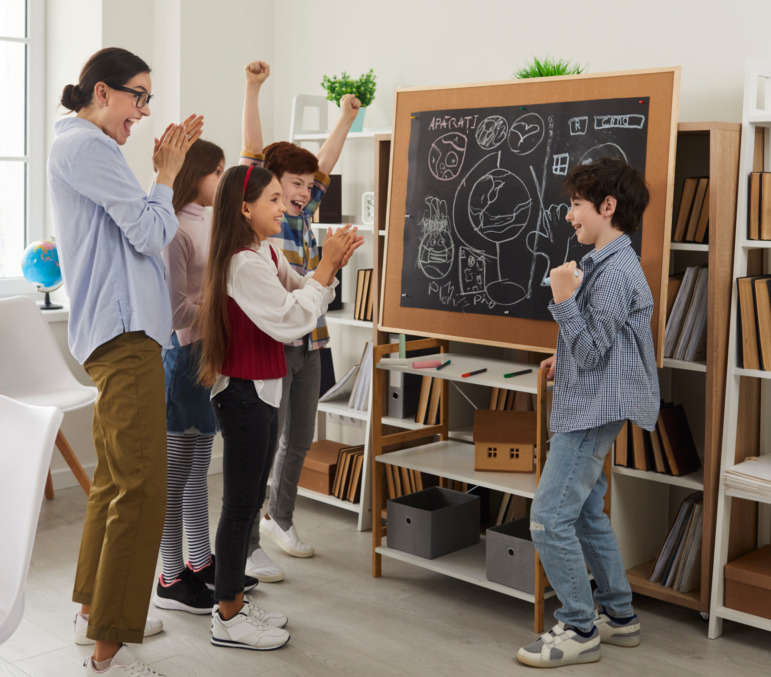 AI replace teachers: Happy teacher and cheerful middle school school students standing in front of classroom black board and applauding classmate