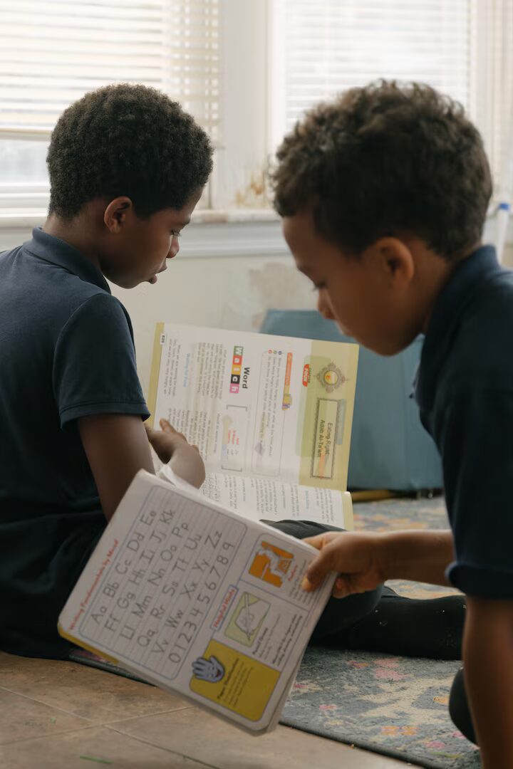 Online school: Two young boys with dark hair sit on the floor reading books