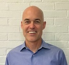 Competency-based innovative high school: Headshot of bald man in light blue shirt in front of white brick wall