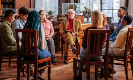 Restorative justice: Group of adults and teens sit in dark wood library in dark wooden chairs in a circle