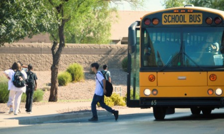 Arizona school vouchers: Elementary school kids getting off a big, yellow school bus and walking along a sidewalk away from camera