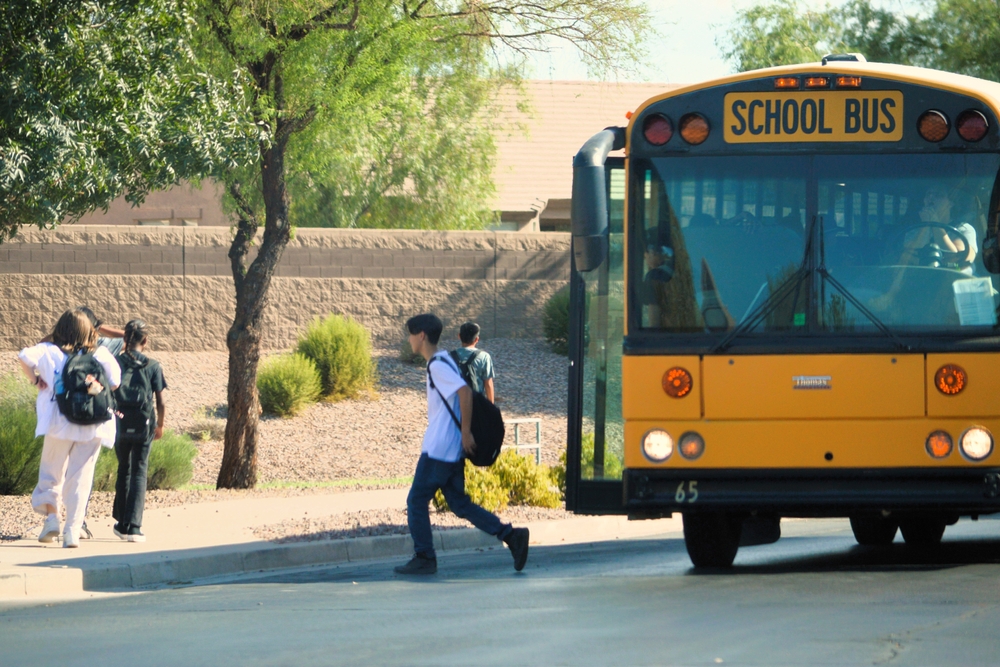 Arizona school vouchers: Elementary school kids getting off a big, yellow school bus and walking along a sidewalk away from camera