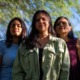 Latino gun reform Arizona: Thre Latino women with long, dark hair stand together facing camera with green tree foliage in the background