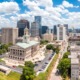 Free college tuition: Long view of traditional off-white multi-story building surrounded by a parking lot, other city buildings and skyscrapers.