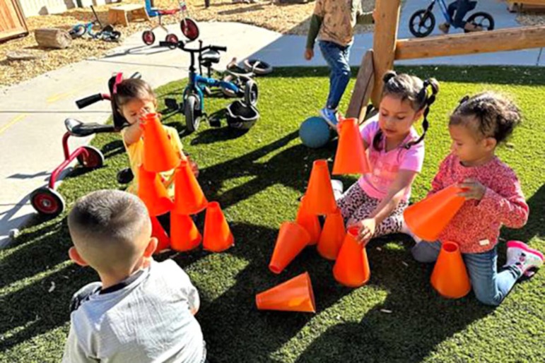 Childcare subsidies: 4 preschool students play on grass with large orange blocks