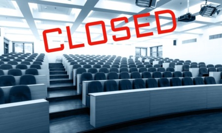 Colleges closing: Empty, large, tiered-seating college lecture hall in black and white with word "CLOSED" in all caps red text angled across the image