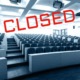 Colleges closing: Empty, large, tiered-seating college lecture hall in black and white with word "CLOSED" in all caps red text angled across the image