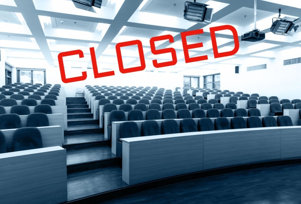 Colleges closing: Empty, large, tiered-seating college lecture hall in black and white with word "CLOSED" in all caps red text angled across the image