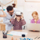 EdTech R&D: Elementary students in vr headsets and at laptop next to 3d printer sit and stand next to at desks while teacher lens in to help them