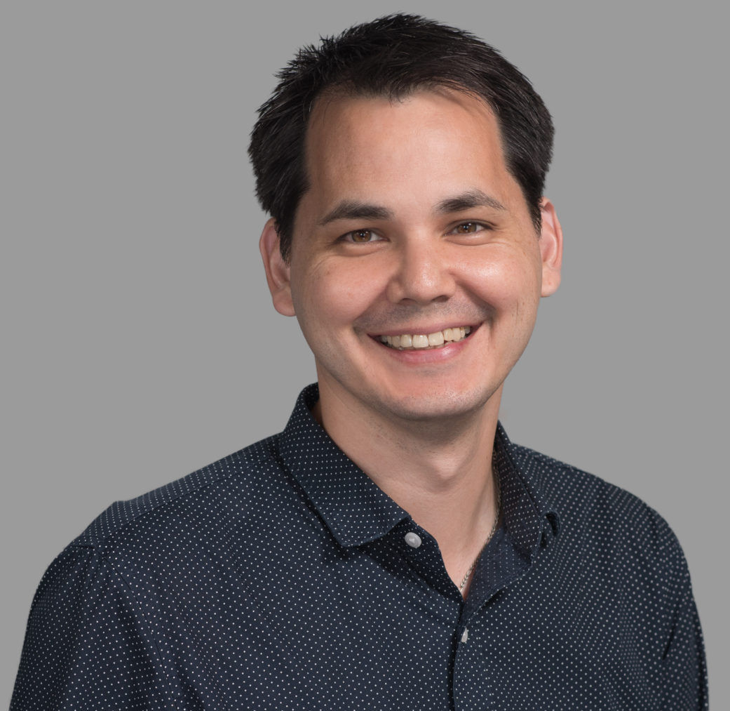 Headshot of man with dark wavy hair in charcoal business shirt smiling broadly into camera