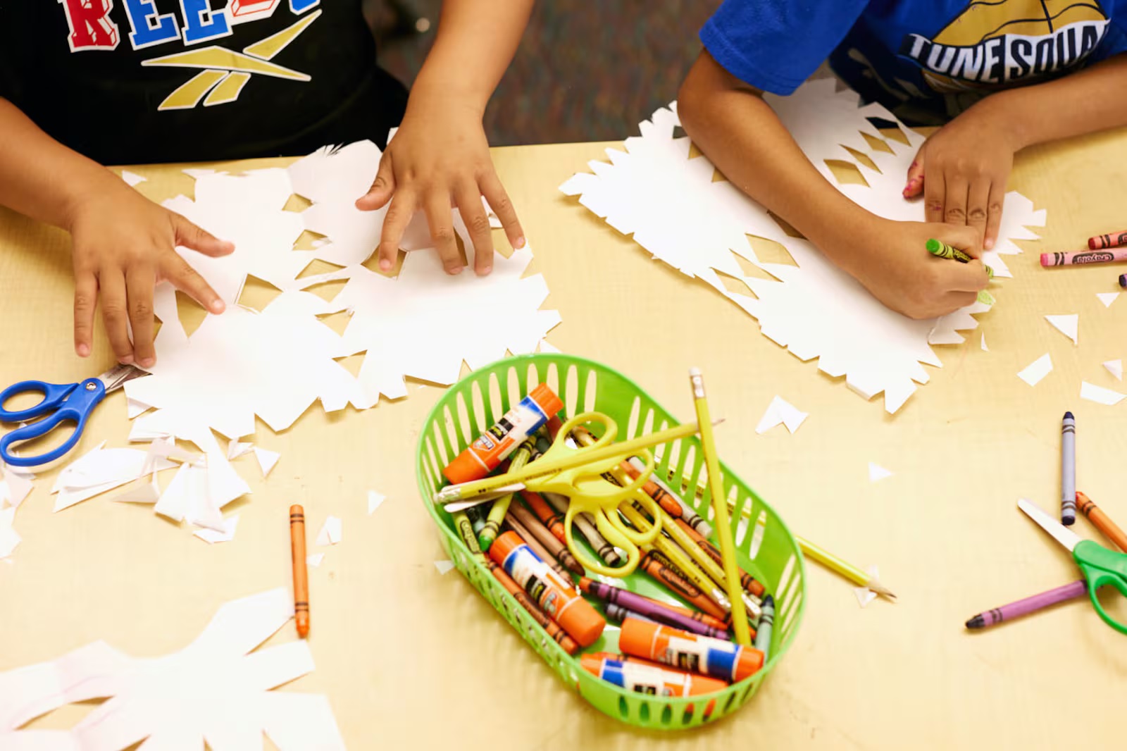 Teacher expenses, what teachers buy for their classrooms with their own money: hands of children working at table with crayons, pencils, glue, scissors and paper