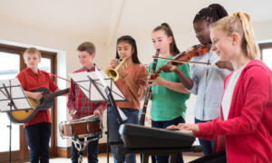 educational opportunity gap: 5 young teen stand and sit playing different musical instruments together