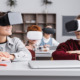 EdTech report: Happy elementary classmates looking at each other while sitting at desks gaming in vr headsets in classroom