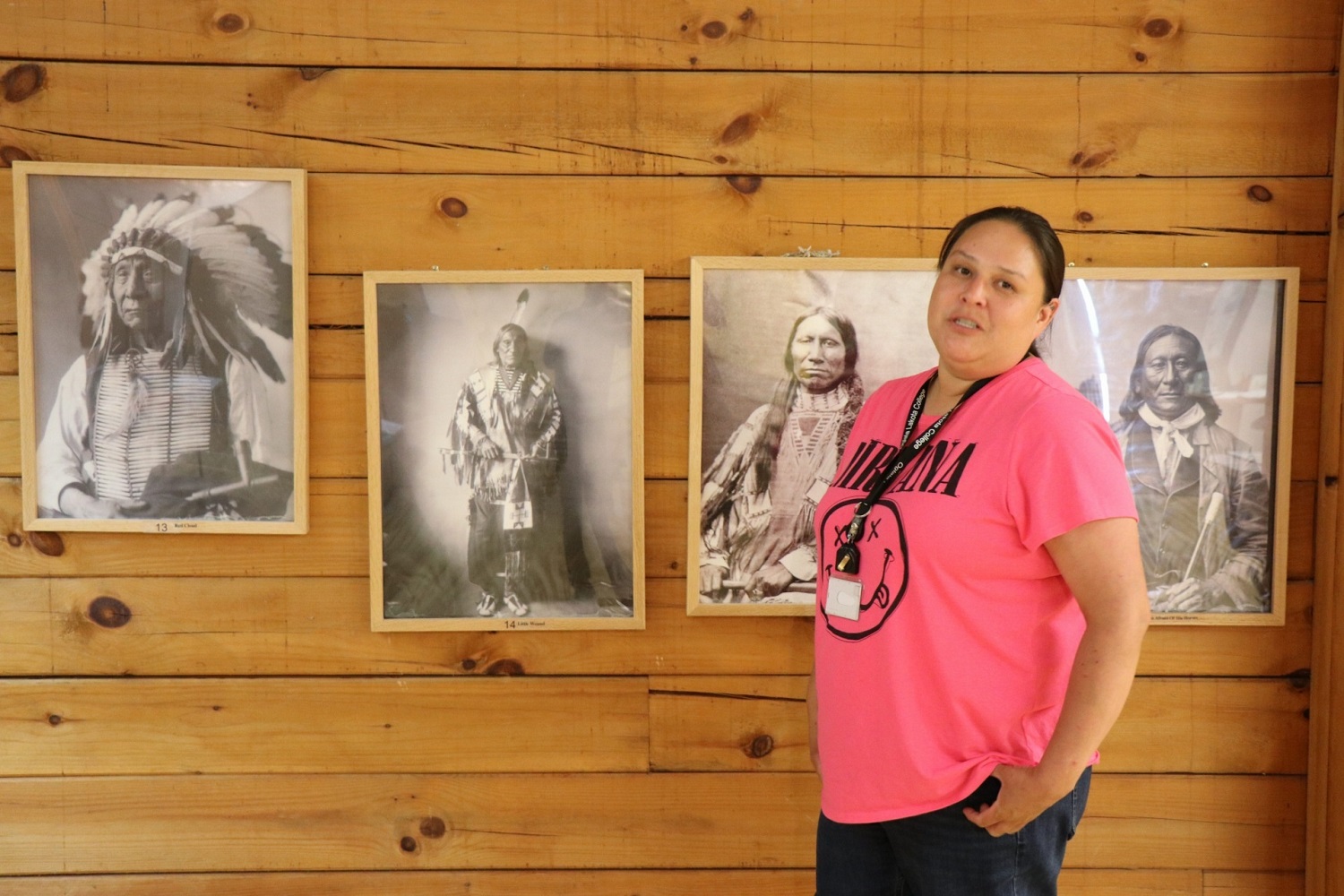 Tribal college campuses are falling apart: woman standing in front of old pictures of ancestor Native Americans on wooden wall