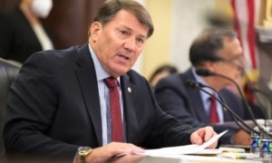 Shut down US DOE: Sebn. Mike Rounds, Reb. from S. Dakota -- a middle -aged man in navy suit and light blue shirt with red tie sits at dark wood table speaking into a microphone.