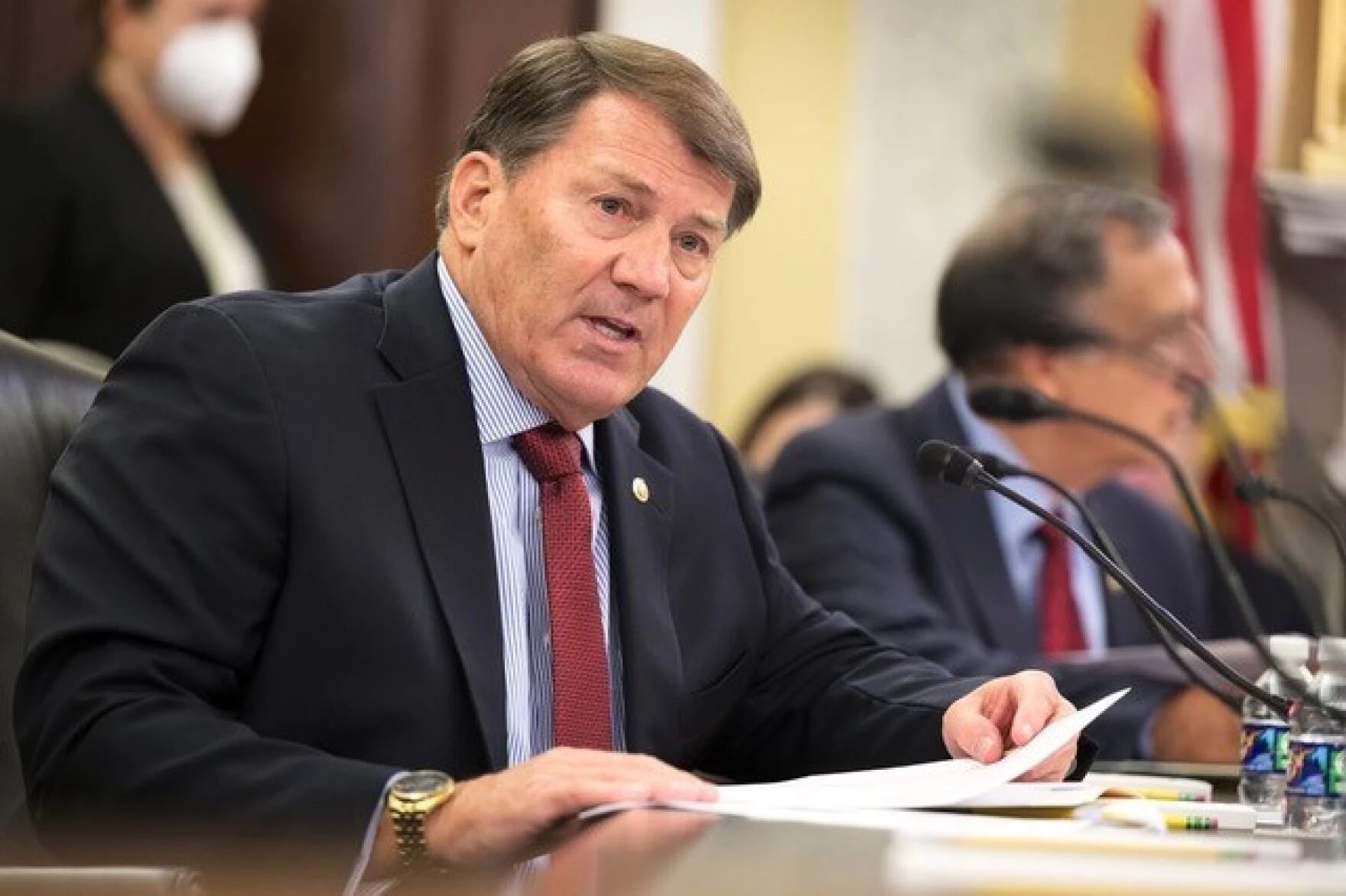 Shut down US DOE: Sebn. Mike Rounds, Reb. from S. Dakota -- a middle -aged man in navy suit and light blue shirt with red tie sits at dark wood table speaking into a microphone.