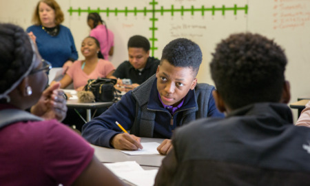 Data science curriculum: Several students sit at classroom desks with teacher in background and a graph on the whiteboard