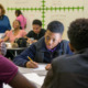 Data science curriculum: Several students sit at classroom desks with teacher in background and a graph on the whiteboard