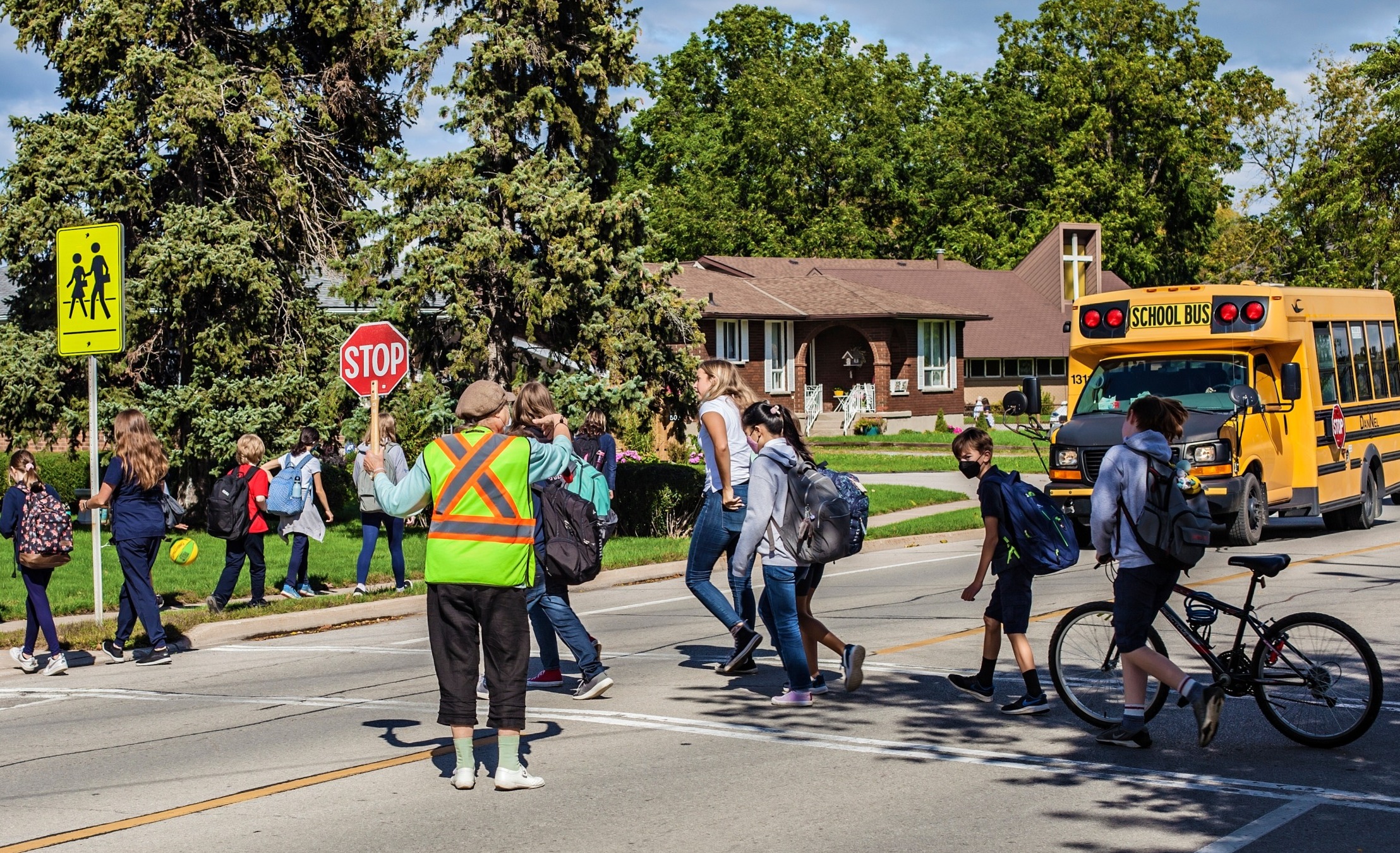 Cannabis dispensary near schools:A few dozen upper elementary and middle school age students walk on sidewalk and in crosswalk in front of red school building and yellow school bus