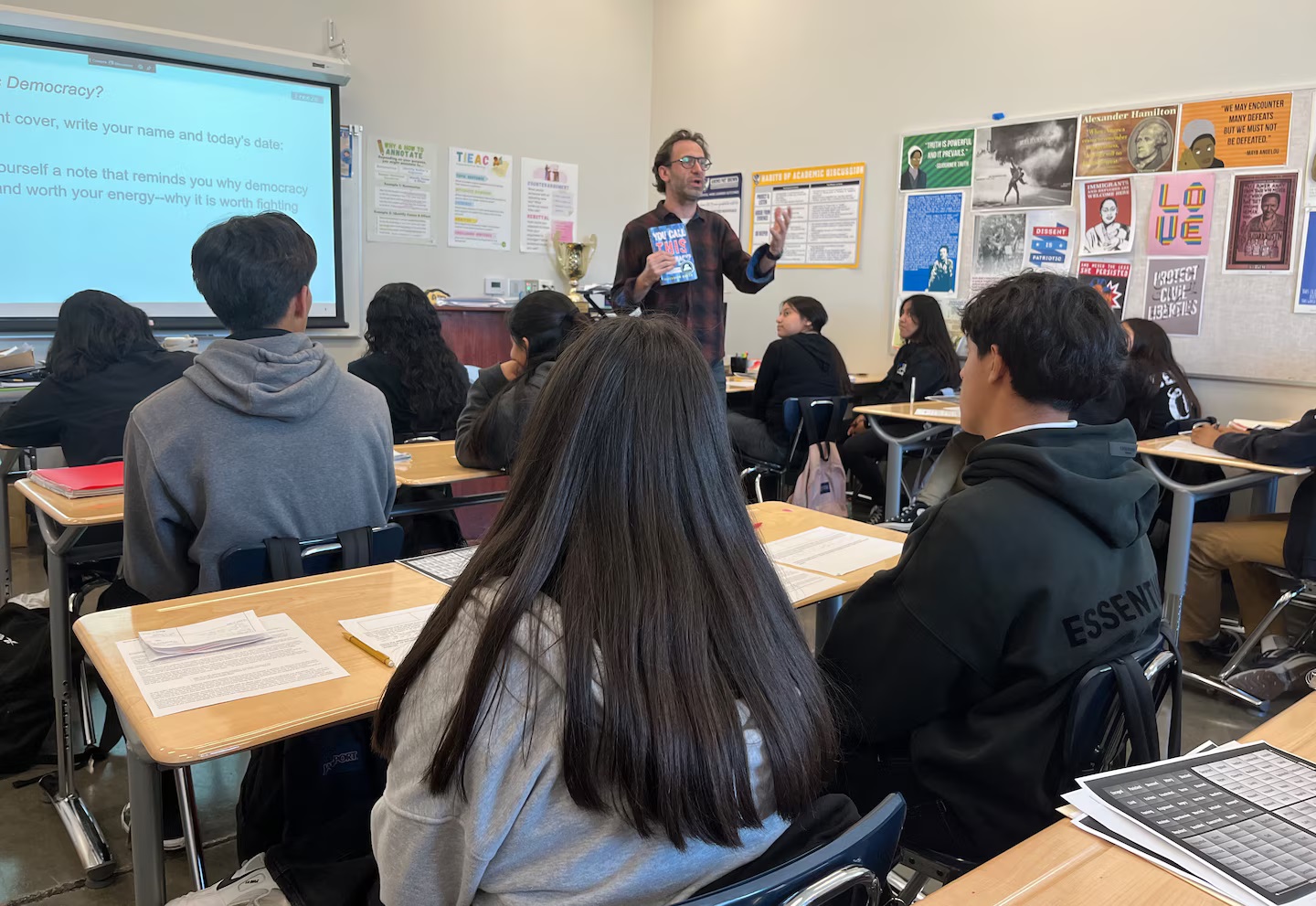 Teachers toss their lesson plans, give students the floor to grapple with Trump win: teacher holding a book while talking to the class