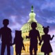 Child tax credit: Dome of US Capitol lit up against cloudy purple night sky with deep, dark purple silhouette of 6 children of various heights standing holding ands facing the Capitol overlaid in foreground.