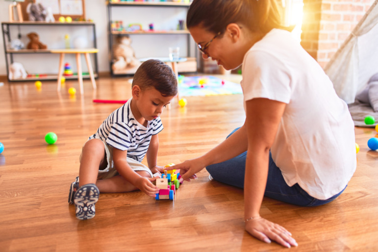 Childcare-Preschool dark future: Female teacher sits on floor playing with preschool boy in classroom