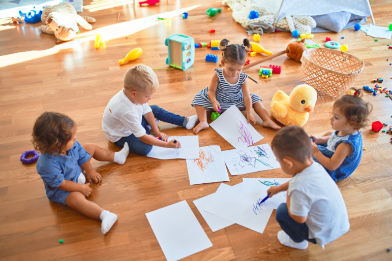 Childcare-Preschool dark future: Six toddlers sit on preschool classroom floor coloring on sheets of white paper