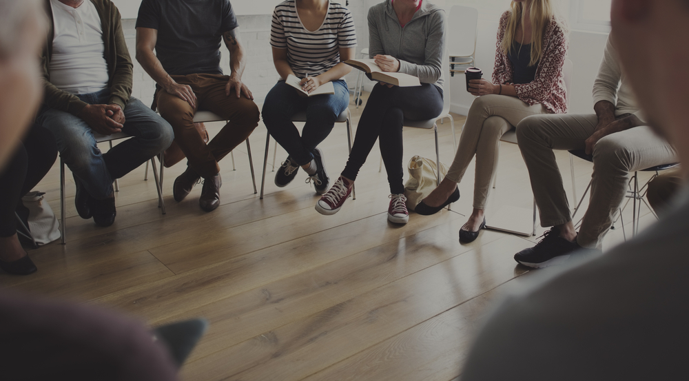 College listening cohort: Closeup of group of people sitting in a circle in room with light wood floor