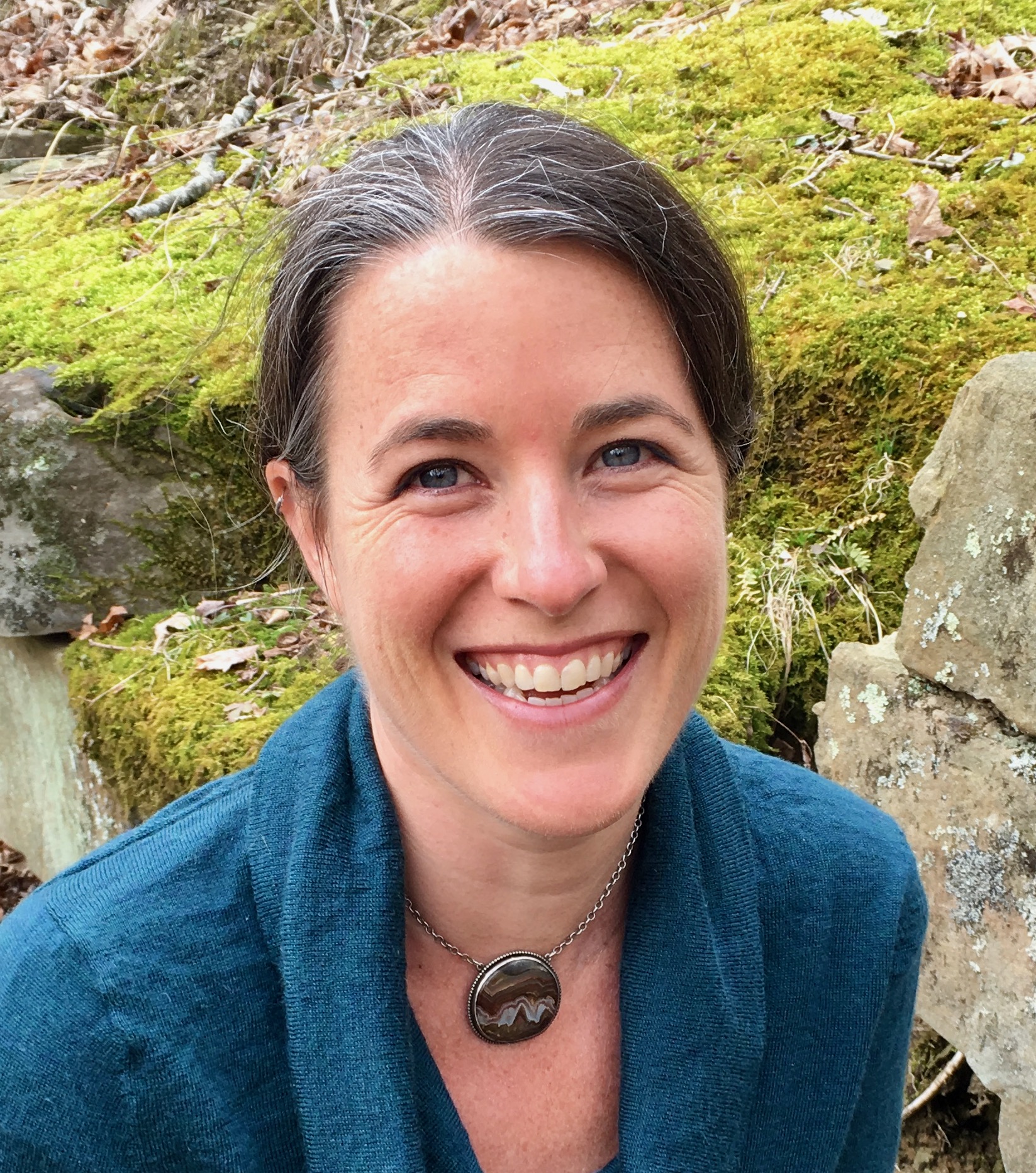 College listening cohort: Headshot woman with brown hair pulled back in teal shirt in front of greenery