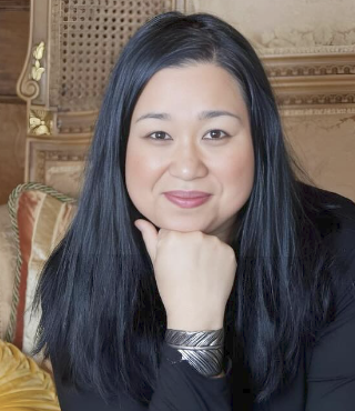 College listening cohort: Headshot Asian woman with long black hair in dark top seated with chi non hand