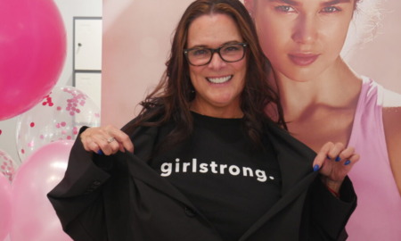 Girlstrong fashion: Young woman with long dark hair and dark-framed glasses wears black t-shirt with "Girlstrong" in white letters on chest