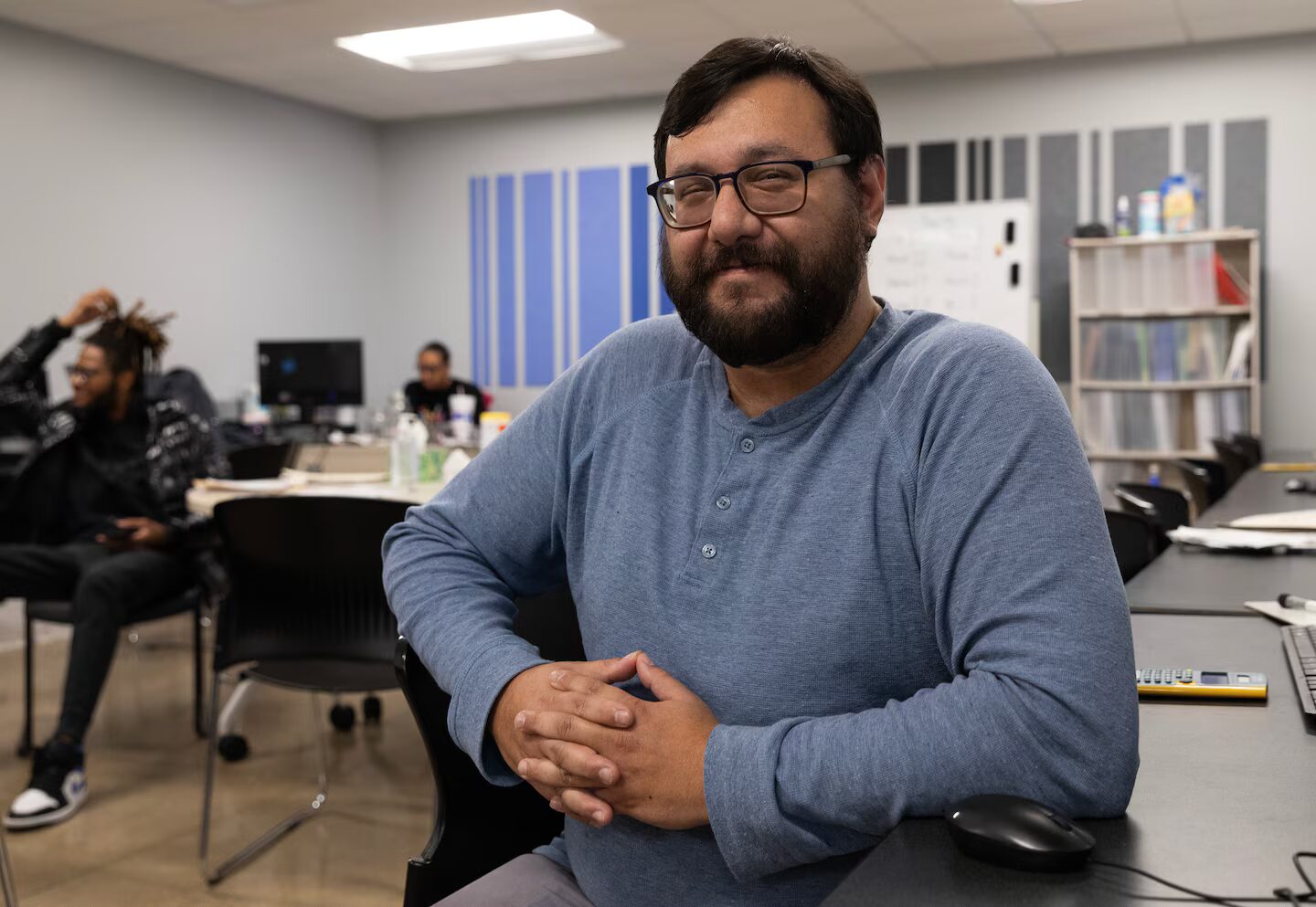 High school drop-out: Man with short brown hir and full beard wearing light blue sweater sits in classroom